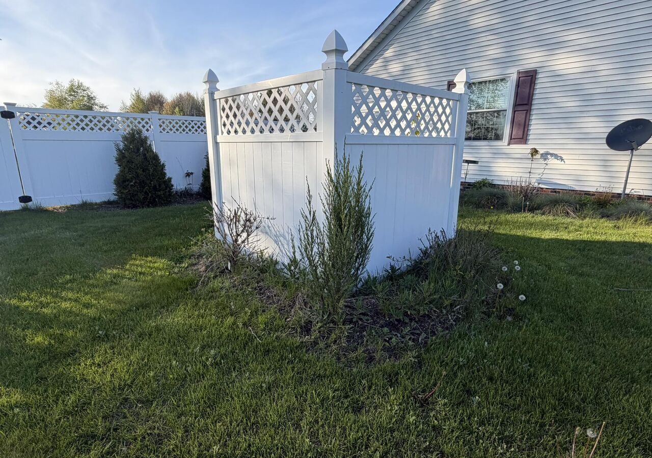 White vinyl privacy fence with lattice top surrounding a small garden bed in a sunny backyard.