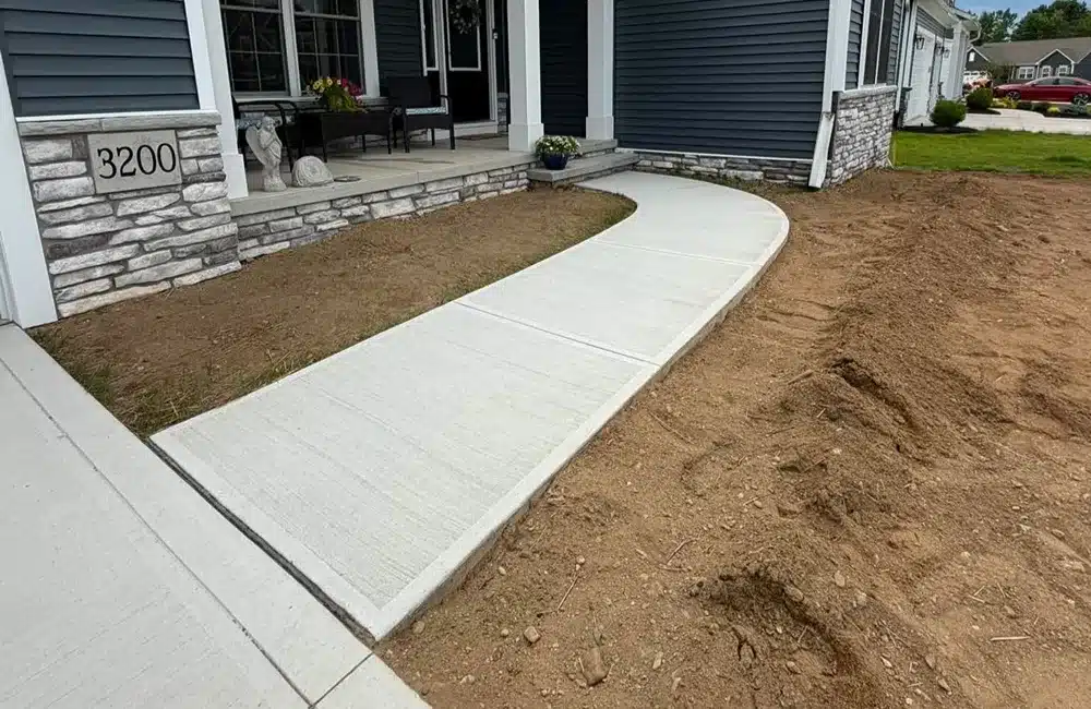 Curved concrete walkway to the front porch, with a stone-faced foundation and house number 3200; dirt yard on the right.